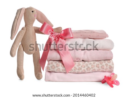 Stack of baby girl's clothes, pacifier and toy bunny on white background