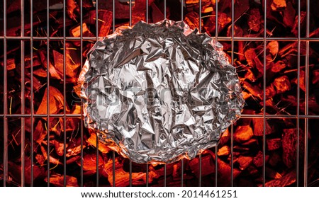 Aluminum foil on  grate over hot pieces of coals. Top view.