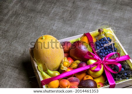Variety of ripe fruits and berries are beautifully stacked in wooden box tied with pink ribbon. Dark background. Food delivery, gift fruit set. Concept of healthy eating. Copy space. Selective focus. Royalty-Free Stock Photo #2014461353