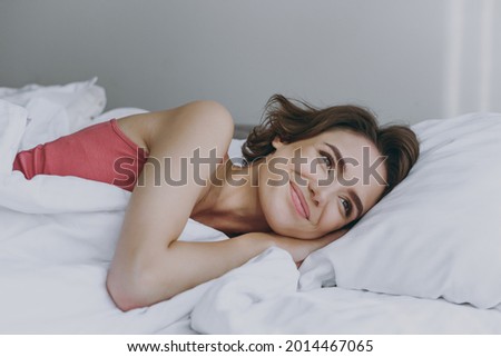 Calm minded caucasian happy young woman 20s wear pajamas tank shirt lying in bed lies wrap covered under blanket duvet on pillow rest relax indoors at home. Good mood night morning bedtime concept. Royalty-Free Stock Photo #2014467065