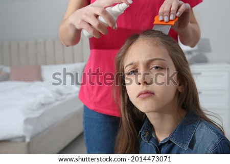 Mother using nit comb and spray on daughter's hair at home. Anti lice treatment