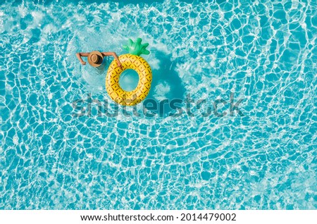 Top view of a young female in swimsuit bikini in a straw hat on blue swimming pool waves background with big inflatable Yellow Pineapple tube. Chill out a summer vacation in luxury resorts concept. Royalty-Free Stock Photo #2014479002