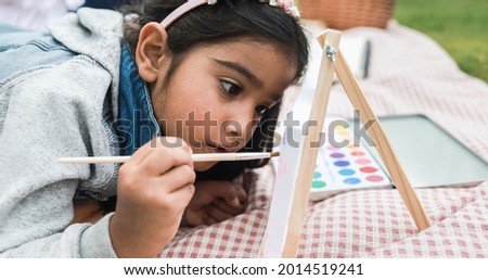 Happy indian little girl having fun painting outdoor at city park - Main focus on girl face