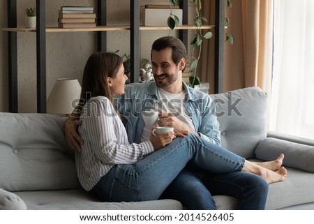 Loving spouses relax on sofa chatting holding cups of tea, having pleasant conversation, enjoy romantic date, discuss joint future plans dreaming together resting at modern home. Leisure, love concept Royalty-Free Stock Photo #2014526405