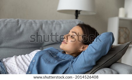 Close up beautiful serene carefree young woman relaxing on sofa, female put hands behind head closed eyes smile breath fresh air in modern living room. Stress-free day off, recreation, comfort concept Royalty-Free Stock Photo #2014526408