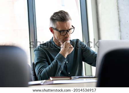 Serious busy elegant mature businessman corporate leader successful ceo executive manager thinking of online business planning financial market strategy, using laptop computer sitting at office table. Royalty-Free Stock Photo #2014536917