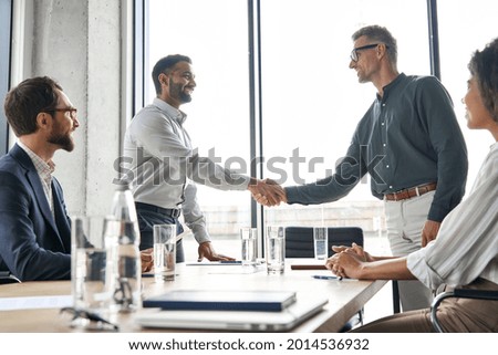 Two happy diverse professional business men executive leaders shaking hands after successful financial deal at group board office meeting. Trust agreement company trade partnership handshake concept. Royalty-Free Stock Photo #2014536932