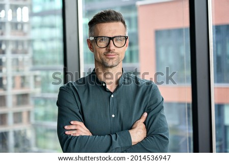 Smiling confident mature businessman looking at camera standing in office. Elegant stylish corporate leader successful ceo executive manager wearing glasses posing for headshot business portrait. Royalty-Free Stock Photo #2014536947