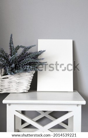 Canvas on shelf with lavender flowers in white basket, interior decor, grey wall. Blank picture. Stretched cotton canvas