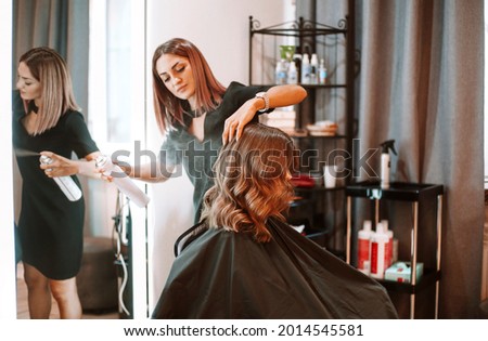 Young female hairdresser fixing hair of gorgeous smiling woman with hairspray. Hairdress and beauty concept Royalty-Free Stock Photo #2014545581