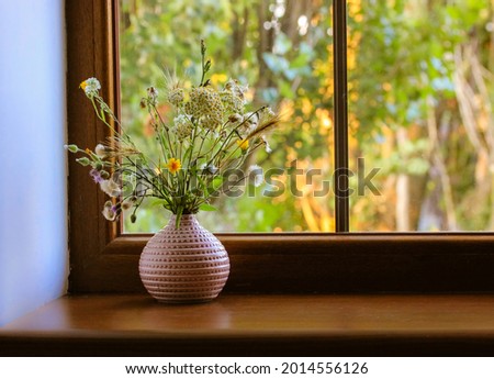 Bouquet of different wildflowers in a pink vase on a wooden window sill against a window at summer sunny day. Flowers in the home interior. Cosy homy atmosphere. Place for text. Natural background. Royalty-Free Stock Photo #2014556126