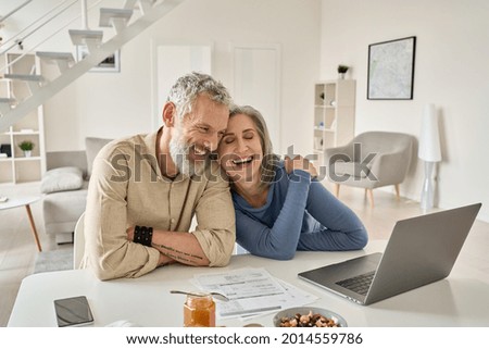 Happy mature older family couple laughing, bonding sitting at home table with laptop. Smiling middle aged senior 50s husband and wife having fun satisfied with buying insurance, paying bills online. Royalty-Free Stock Photo #2014559786