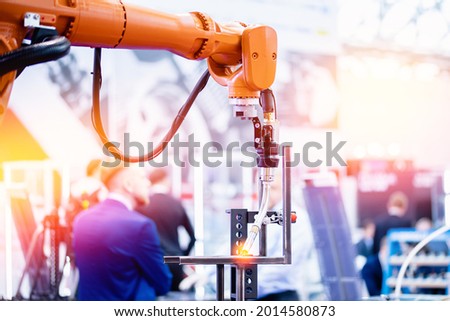 Yellow robot hand performs welding work on metal structures industrial automatic factory, light background.