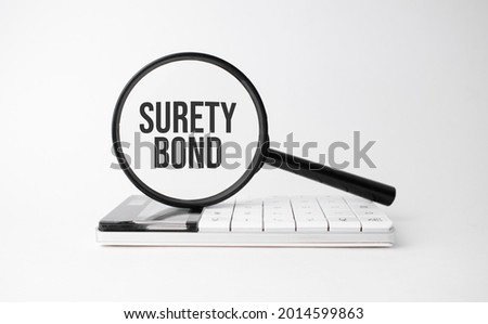 Finance and business concept. On a white background lies a calculator and a magnifying glass with the inscription - Surety Bond Royalty-Free Stock Photo #2014599863