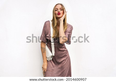 white background portrait of stylish woman posing at white background wearing polka dot silk dress bright make up and trendy accessorizes. Sending air kisses, playfully mood. Royalty-Free Stock Photo #2014600907