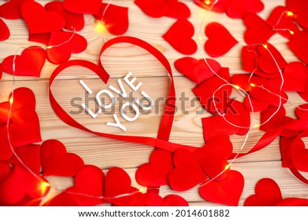 White letters congratulations on Valentine's Day.Happy holiday of lovers men and women.Top view of many beautiful red hearts made of ribbon on wooden background.I love you.February 14 in winter