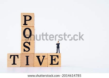 positive thinking symbol. miniature businessman on Wooden cubes with words 'positive' on white background.