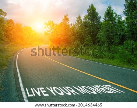 Live your moment, concept photo of asphalt road. Encouraging quote on road. Summer forest landscape with curved highway. Inspirational quote banner. Motivational card. Life mastermind concept