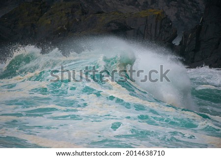 An angry turquoise green colour massive rip curl of a wave as it rolls along a beach. The white mist and froth from the wave are foamy and fluffy. The Atlantic Ocean in the background is deep blue. 