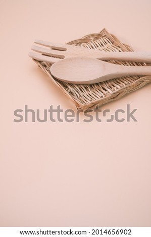 A vertical shot of wooden spoon and fork on a flat wicker basket isolated on light cream background