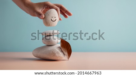 Enjoying Life Concept. Harmony and Positive Mind. Hand Setting Natural Pebble Stone with Smiling Face Cartoon to Balance. Balancing Body, Mind, Soul and Spirit. Mental Health Practice Royalty-Free Stock Photo #2014667963