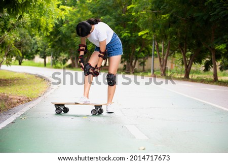 Woman surf skate board putting on elbow protector pads on her arm and wearing wrist guards and Safety.
