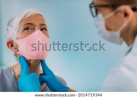 Thyroid gland medical exam. Endocrinologist examining nack of a senior woman with thyroid disease symptoms. Wearing protective mask.   Royalty-Free Stock Photo #2014719344