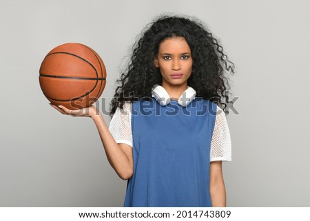 Pretty young black woman balancing a basketball on her hand posing looking at camera with a serious expression and headphones around her neck