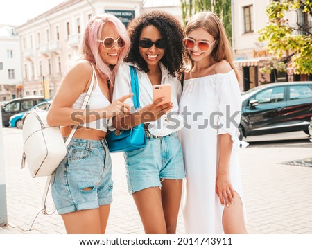 Three young beautiful smiling hipster female in trendy summer clothes.Sexy carefree multiracial women posing in the street.Positive models in sunglasses. Looking at smartphone screen.Using phone apps Royalty-Free Stock Photo #2014743911