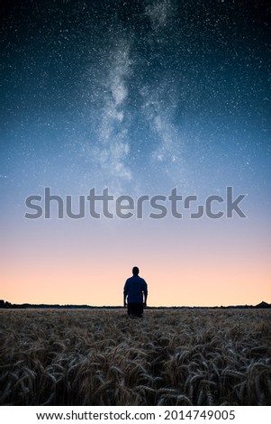 Man standing on wheat field under the stars of the milky way at night. Man looking at stars and dreaming.