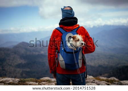 A man in a red jacket, with a dog in a backpack, against the background of the Caucasian mountains, Lago-naki plateau, Russia Royalty-Free Stock Photo #2014751528