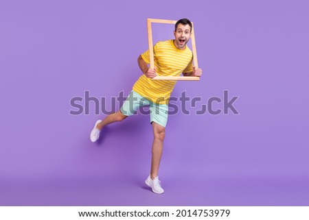 Full length photo of cheerful young happy positive man amazed hold frame isolated on purple color background