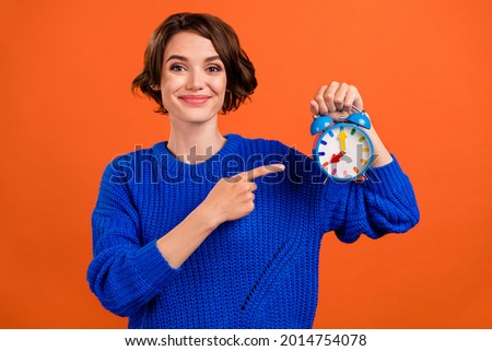Photo of funny brunette young lady point clock wear blue pullover isolated on orange color background