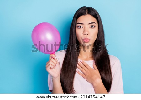 Photo of charming young amazed woman hold hand balloon chest festive isolated on blue color background