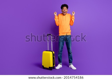 Full body photo of cheerful young happy afro american man winner luggage wear jeans hoodie isolated on purple color background