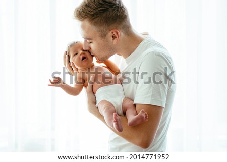 Portrait of handsome young caucasian ather holding his newborn baby girl in hands. Happy dad kissing his infant baby in cheek.