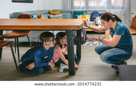 Mother explaining to her children how to protect themselves in an earthquake by getting under the table while preparing emergency backpacks Royalty-Free Stock Photo #2014774235