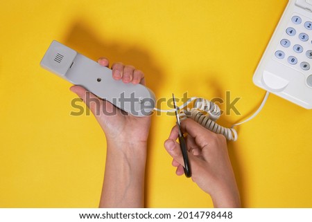Someone cuts the cable from the white wired landline phone Royalty-Free Stock Photo #2014798448