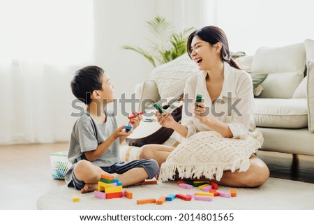 Cute Asian woman and kid playing educational toys together in living room. Mom and son play cubes and laugh Happy family. Young mother and son doing activities together at home. Royalty-Free Stock Photo #2014801565