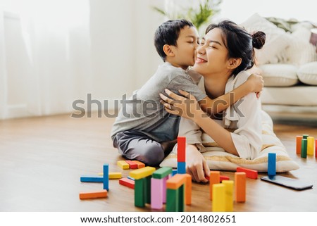 Cute Asian woman and kid playing educational toys together in living room. Boy hugs his mom with love. Happy family. Young mother and son doing activities together at home.