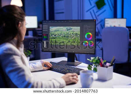 Focused editor retoucher editing color grade on professional computer sitting at desk in creative office at midnight. Freelancer video editor start up new movie project processing audio film montage.