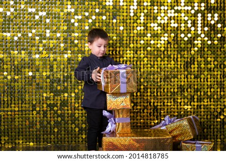 child smiling boy holding gift box on background with gold shiny sequins, paillettes.