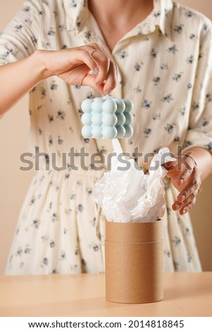 Female hands taking out a blue bubble candle out of a cylinder packaging made of recycled paper