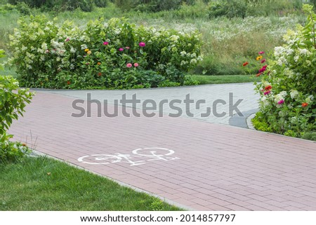 Cycle path in park among flower beds. Pictogram of bicycle on asphalt.
