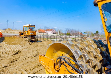 View on road roller with spikes vibrating, compactor is compacting, tamping sand for road foundation at building site. Royalty-Free Stock Photo #2014866158