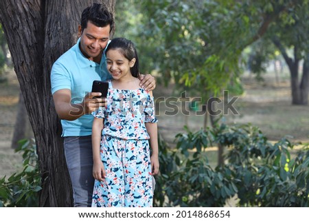 Father and a daughter taking selfies using the smart phone in hand in a park 