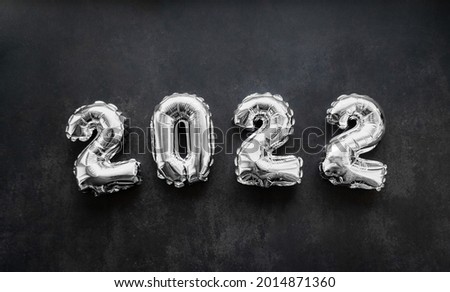 Inflatable shiny silver numbers of the new year 2022 on a dark grey or black background. Copy space