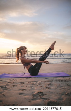 Side view of fit young woman stretching and doing boat yoga pose on the beach. Young yogi woman practicing yoga, doing Paripurna Navasana exercise.