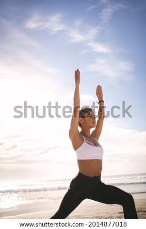 Woman practicing yoga at the beach. Fitness females doing warrior yoga pose at beach. Virabhadrasana posture.