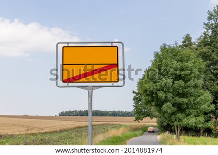a blank traffic sign which you can label yourself. Town exit sign on a street in the background you can see a car. 